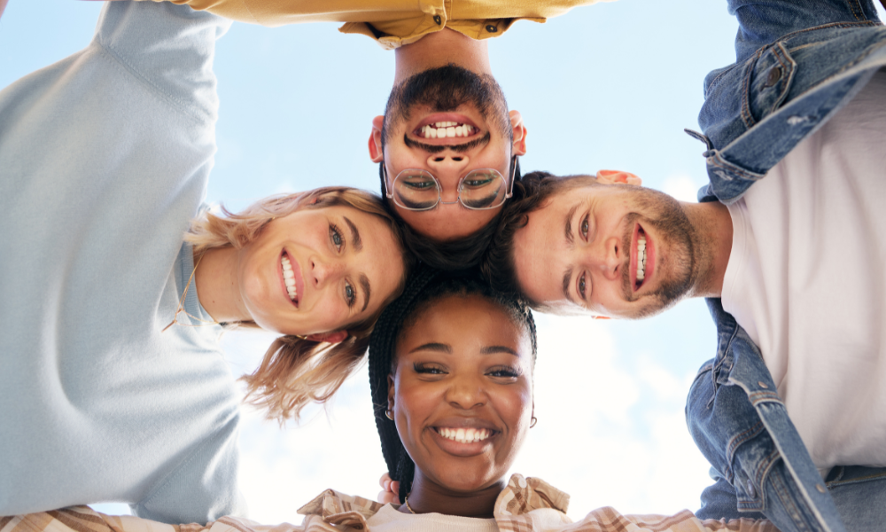 4 College friends with their heads together in a circle talking about college scholarships with April deadlines