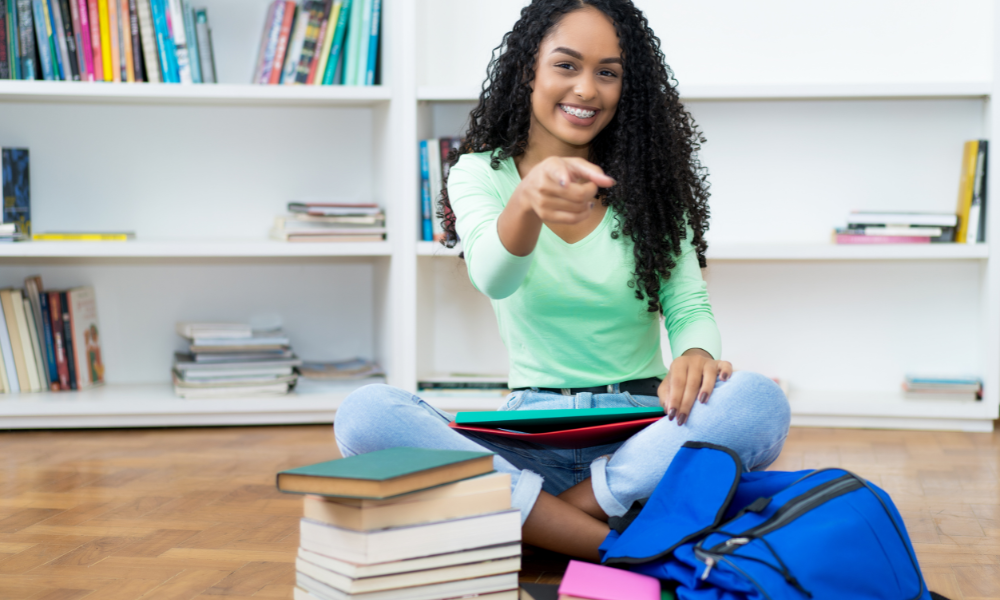 A high school junior sitting down with her books and bookbag on a college campus, virtual programs, head start, Harvard campus, research science institute, financial aid, scholarships, financial need, biomedical sciences, high school seniors, in-person program, Clark scholars program, valuable experience, Boston University, competitive summer camps, competitive program, Indiana University, exceptional high school students, cutting-edge research