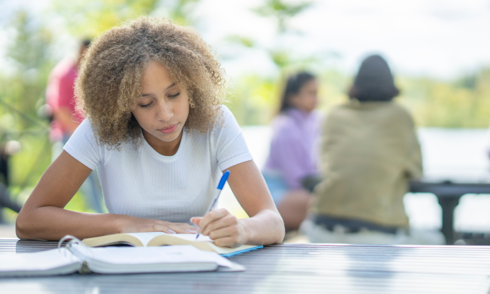 A grad student sitting out reading a scholarship book for scholarships for graduate school, summer scholarships, July scholarships, August scholarships, merit scholarships, financial aid, financial need