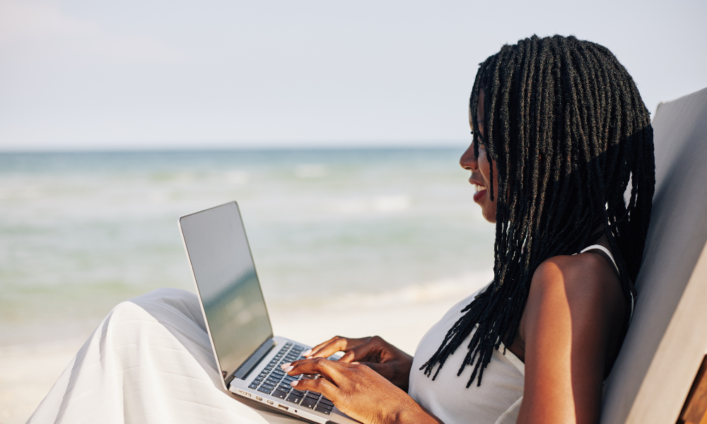 A high school student sitting on the beach with her laptop, applying for scholarships for high school seniors and high school students with end of summer deadlines