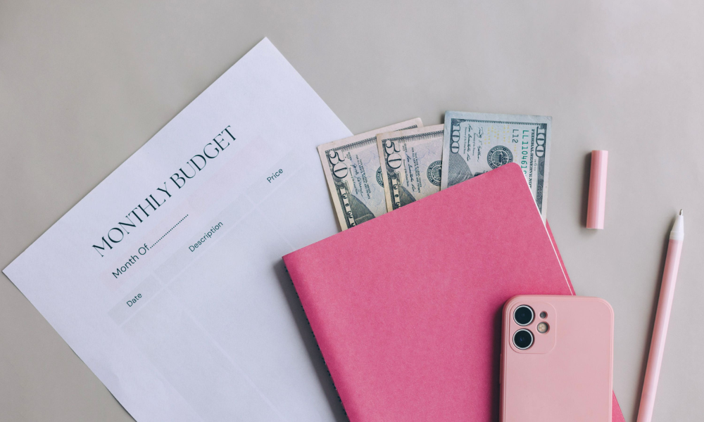 Female college student is sitting at her desk with her student planner, a couple of hundred dollar bills and cell phone and she is trying to calculate her college expenses. She is also applying for quick and easy winter scholarships for the current semester.