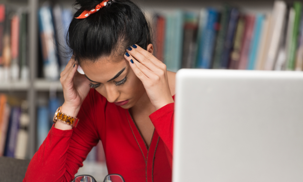 Female college student is rubbing her temples and is frustrated with applying for college scholarships. She just found some common scholarship mistakes in her scholarship application. She believes she should keep a master spreadsheet, clean up her social media, and applying early for scholarships.
