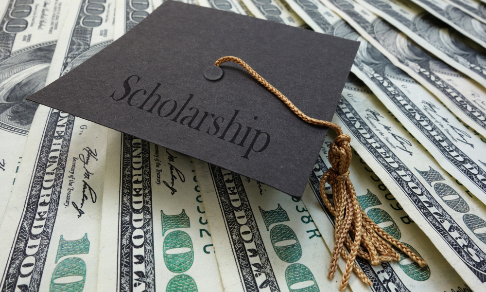 A college senior has her graduation cap sitting on a pile of scholarship money she from the gates scholarship. She is currently applying for June scholarships so she can take out less student loans for medical school