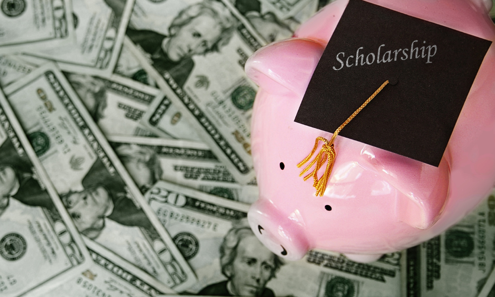 An incoming freshman has a piggy bank on top of a stack of money she won from applying to June scholarships and she also saved money from her part-time job