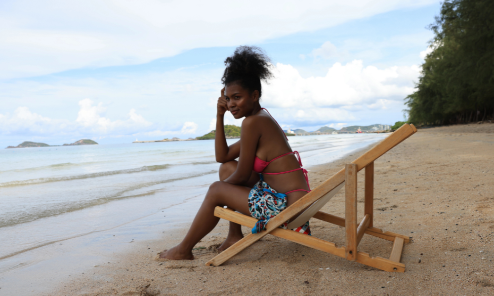 An African American college student is at the beach with her laptop. She is looking for scholarships for minority students, merit scholarships, and late summer scholarships