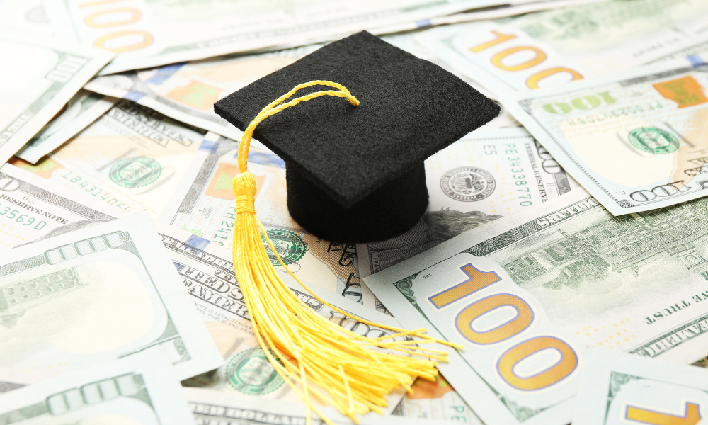 A graduation cap is sitting on a pile of money that the high school senior won from private scholarships, local scholarships, and community service scholarships. The student will continue to apply for scholarships for fall semester.