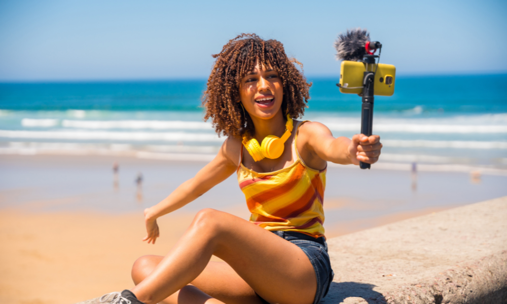A college student at a Big Ten college is sitting on the beach and is shooting content for the Poppi College Ambassador program. She will share the content on her TikTok and IG accounts. She is a brand ambassador for a couple of campus ambassador programs.