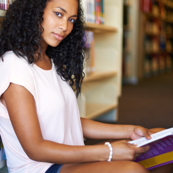 High school girl sitting on the floor of her school's library reading a scholarship book, April scholarships for high school students, easy scholarships, no essay scholarships, teacher recommendation, low-income, learning disability scholarships, income requirements