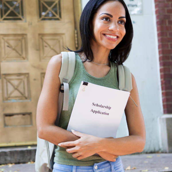 A college woman is walking on her college campus with her book bag and her scholarship application, June scholarships. scholarships with June deadlines, college freshmen, college juniors, college sophomores, high school students, high school seniors, graduating seniors